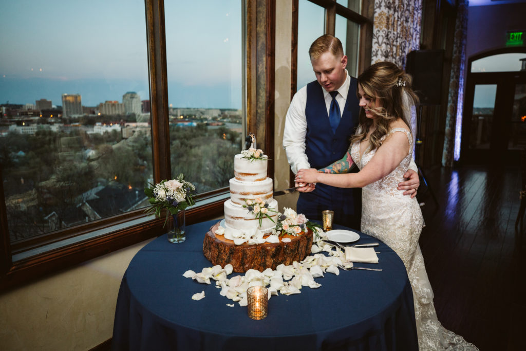 Couple cuts rustic wedding cake inside ballroom reception